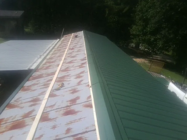 Old rusted panels beside newly installed green metal roofing — Wind Damage Roof Repair by Roofing Brothers in Amity