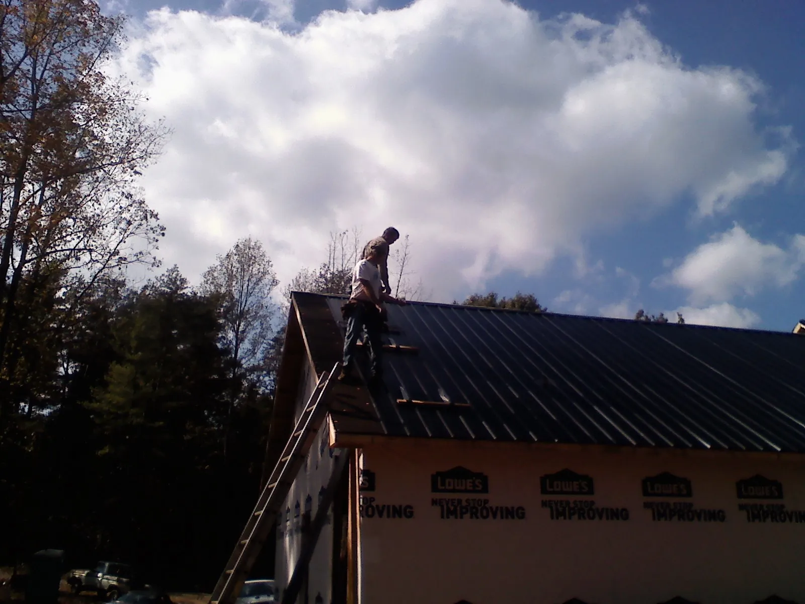 Roofer fastening dark metal panels high against a cloudy sky, from a Roof Inspection job in Amity